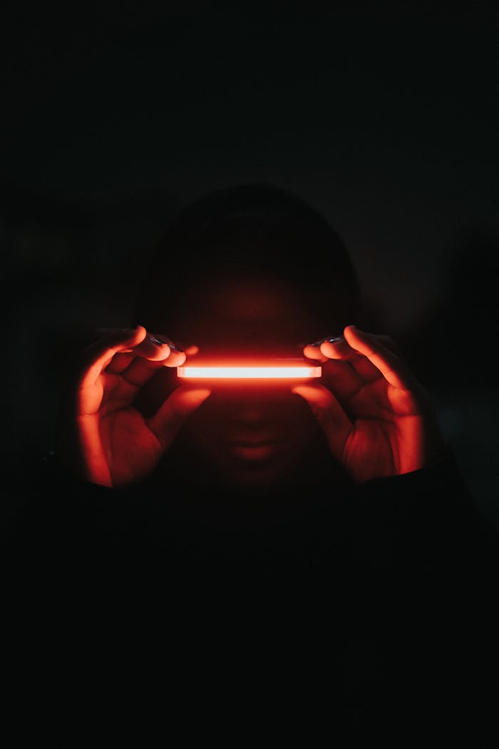 A person enshrouded in darkness holds a glowing red neon light, creating a mysterious atmosphere.