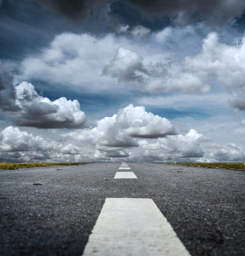A straight road stretched toward a dramatic sky filled with fluffy clouds, creating a sense of journey.
